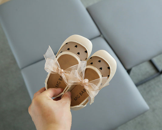 Baby shoes with a bow held by a hand on a light gray surface