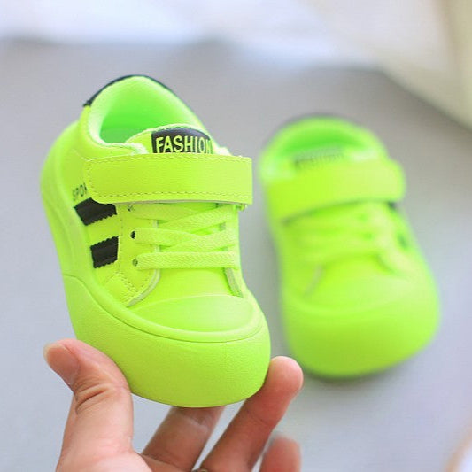 Neon green children's shoes with 'Fashion' label held by a hand on a light gray background