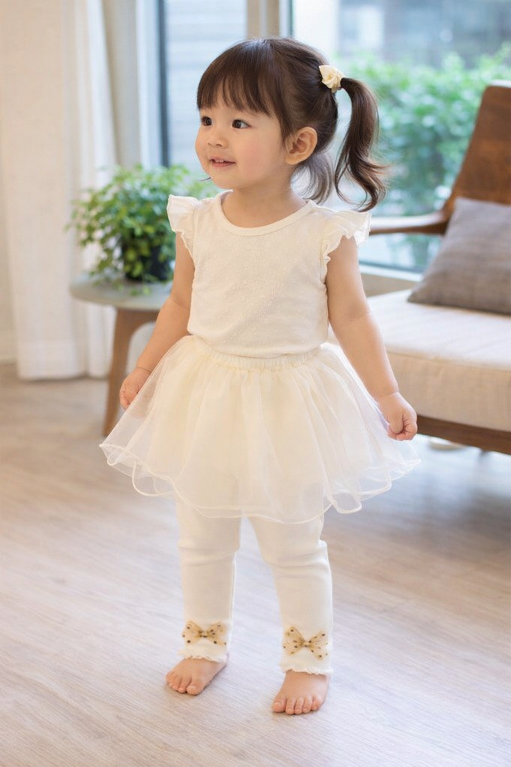 Young girl in a white dress standing in a room with a window and plant in the background