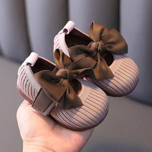 Brown baby shoes with large bows held in a hand against a gray background