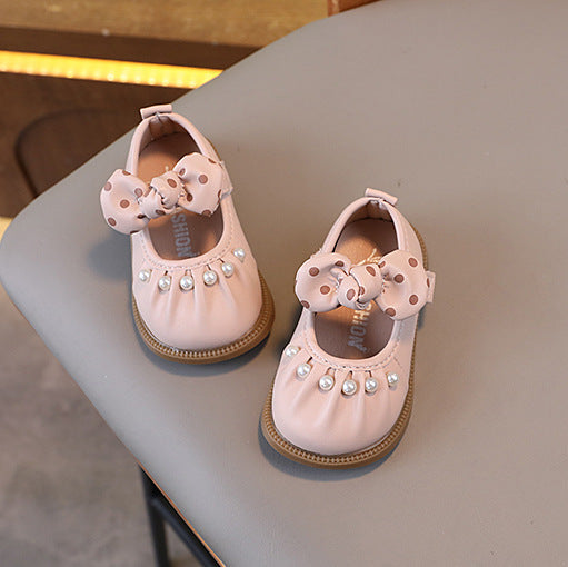 Pair of pink children's shoes with bows and pearls on a gray surface.