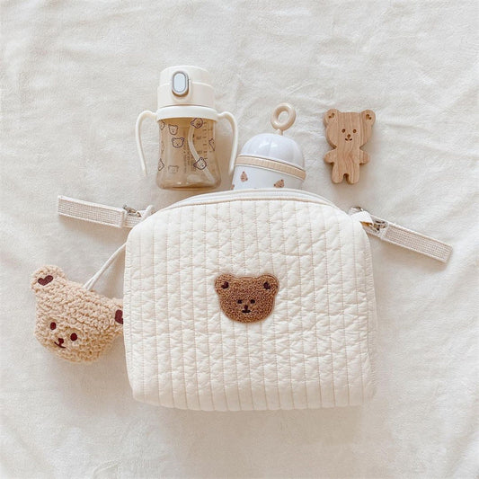 White quilted pouch with bear design, baby bottle, and teether on a soft surface