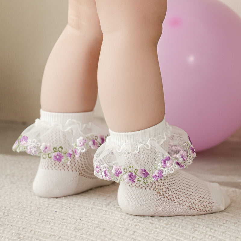 White baby socks with floral embroidery on a neutral background