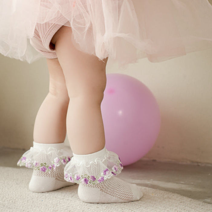 Child wearing white socks with lace trim standing next to a pink balloon.