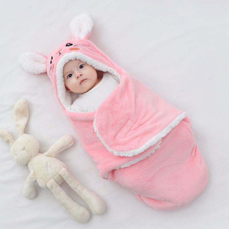 Baby wrapped in a pink swaddle with bunny ears next to a plush toy on a white background