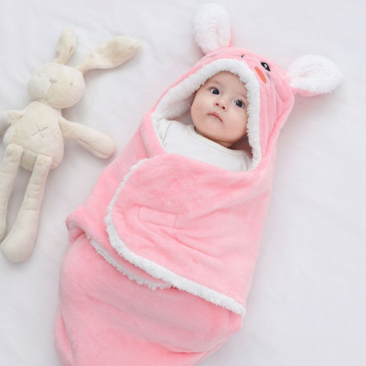 Baby wrapped in a pink swaddle with bunny ears, lying next to a plush toy on a light background