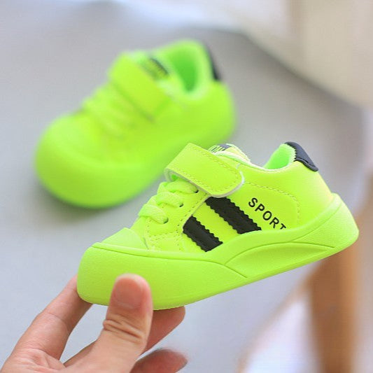 Neon green children's sneakers with black accents held by a hand on a light background