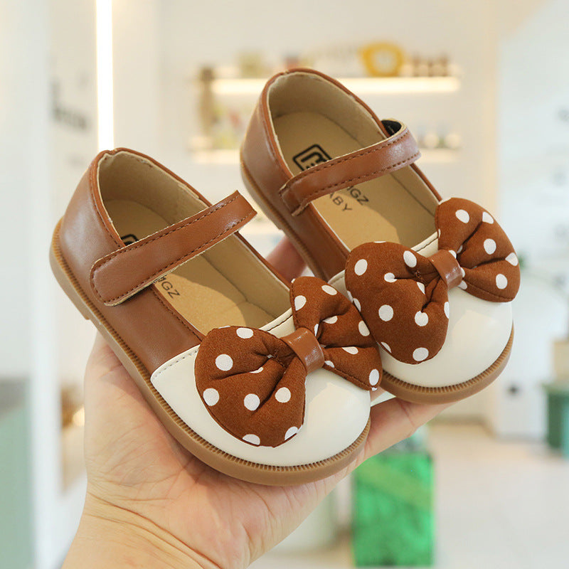 Pair of brown children's shoes with polka dot bows held in a hand.