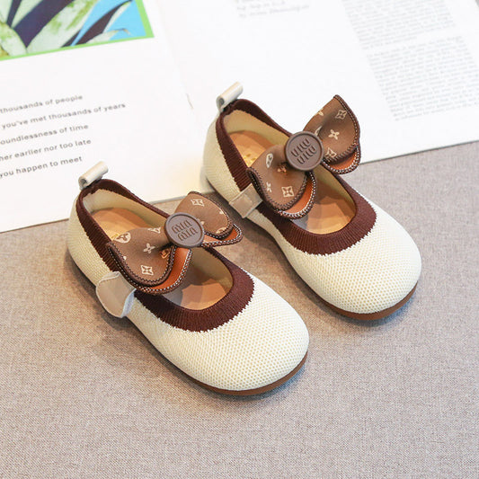 Pair of white and brown shoes with bow details on a textured surface.