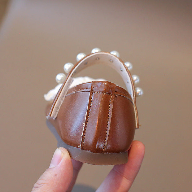 Brown sandal with pearl details held by a hand against a neutral background