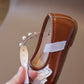 Brown shoe with white lace and pearls held by a hand against a neutral background