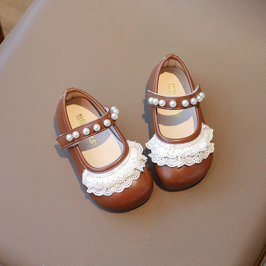 Pair of brown children's shoes with white lace and pearl details on a beige surface