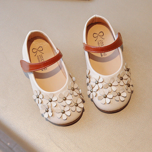 Pair of white children's shoes with floral designs on a beige surface