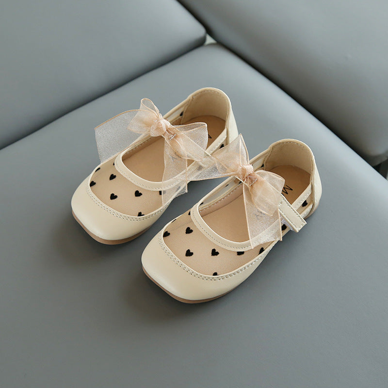 Beige children's shoes with heart patterns and ribbons on a gray surface