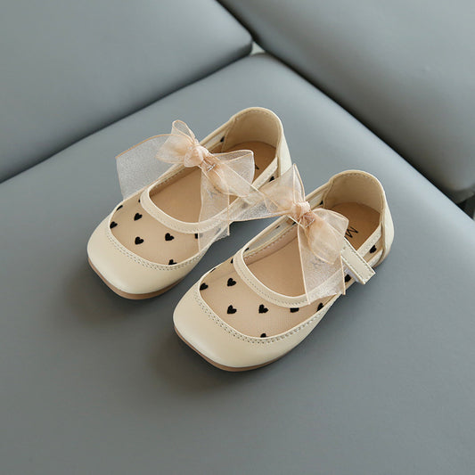 Beige children's shoes with heart patterns and ribbons on a gray surface