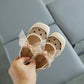 Baby shoes with a bow held by a hand on a light gray surface