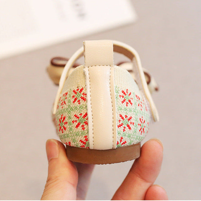Small sandal with floral pattern held by a hand against a neutral background