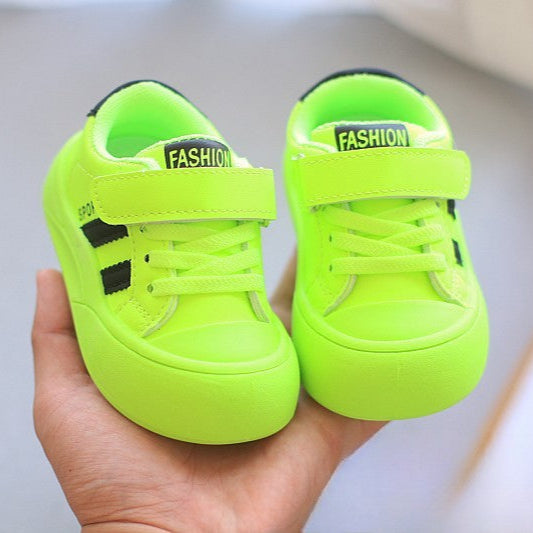 Neon green children's shoes with 'Fashion' label held in a hand against a neutral background