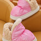 Pink and beige slippers with fluffy texture on a brown chair.