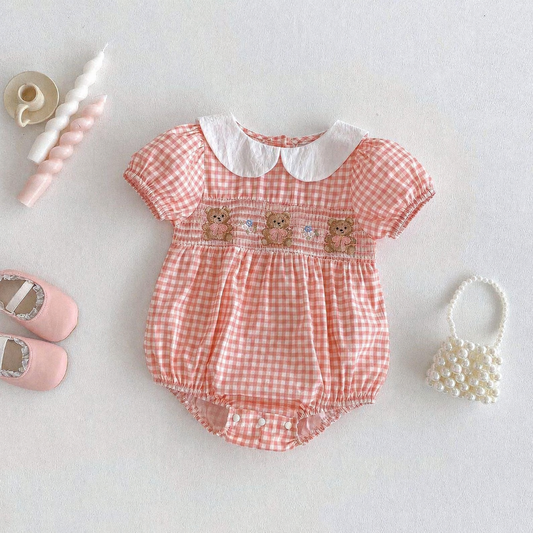 Pink gingham baby romper with teddy bear design on a light gray background