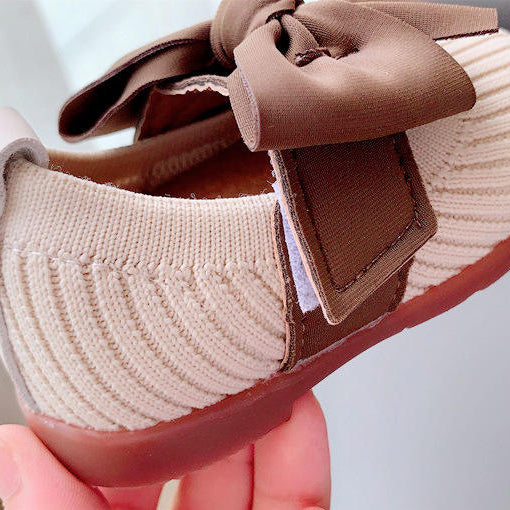 Baby shoe with a brown bow held by a hand on a light background