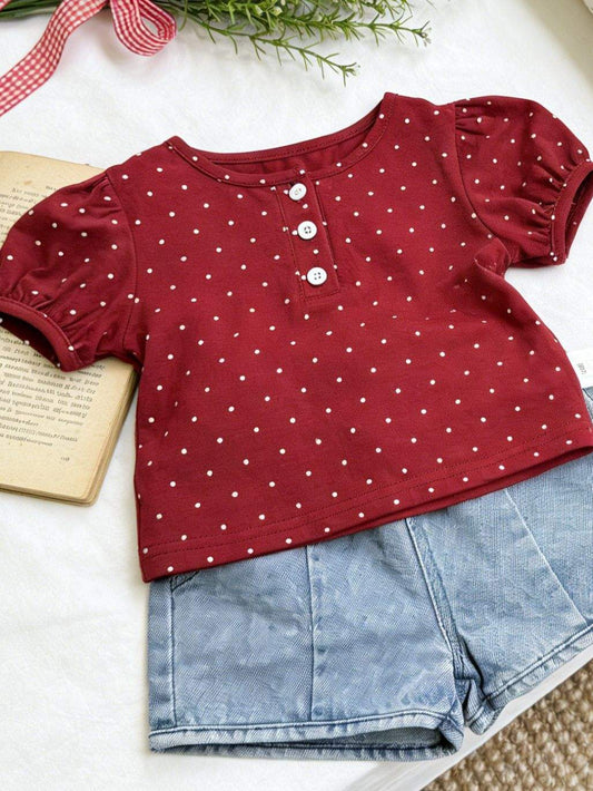 Red polka dot top with blue shorts on a white surface