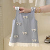 Light blue sleeveless top with bow details held by a hand against a neutral background