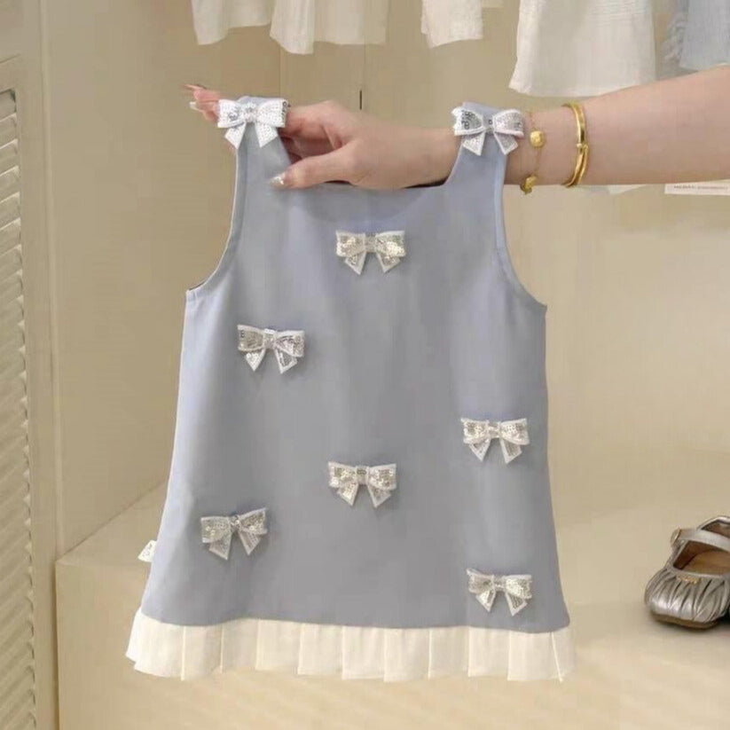 Light blue sleeveless top with bow details held by a hand against a neutral background