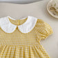 Yellow checkered dress with white collar on a light surface