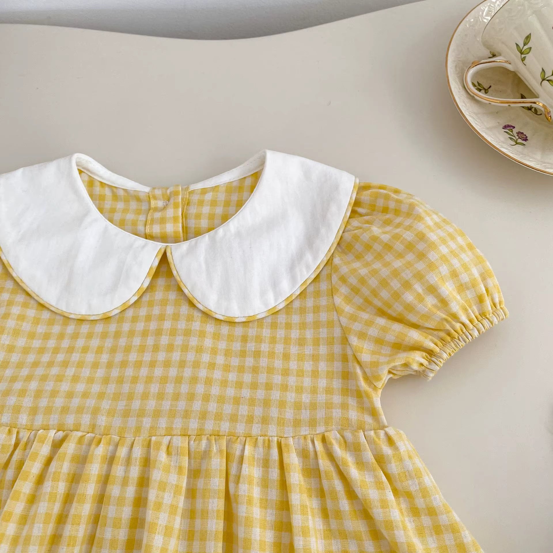 Yellow checkered dress with white collar on a light surface