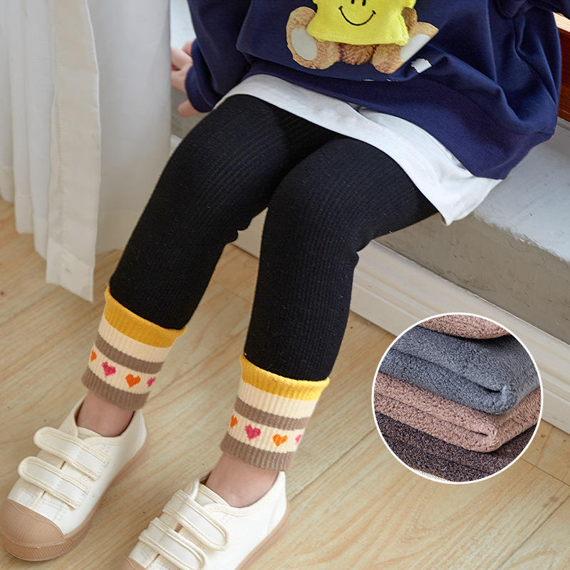 Child wearing black leggings with colorful striped cuffs, sitting on a wooden floor.