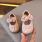 Pair of pink children's shoes with decorative bows held by a hand on a neutral background