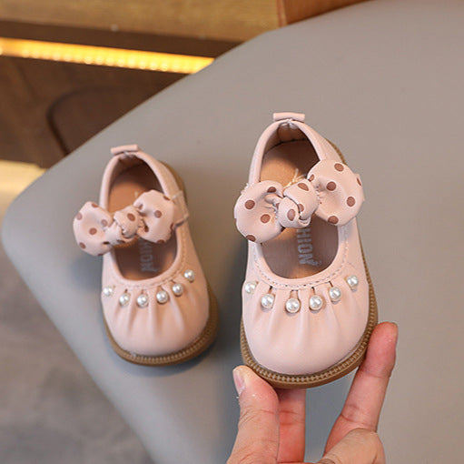 Pair of pink children's shoes with decorative bows held by a hand on a neutral background