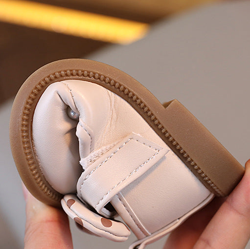Small white boot with brown trim held by a hand against a neutral background