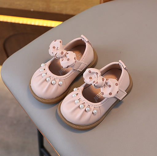 Pair of pink children's shoes with decorative bows on a light surface.