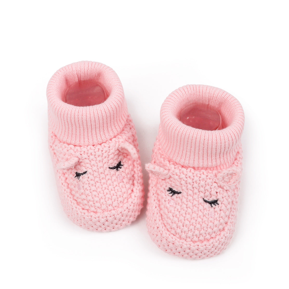 A pair of pink knit baby booties with embroidered sleeping faces on the front, shown on a clean white background.