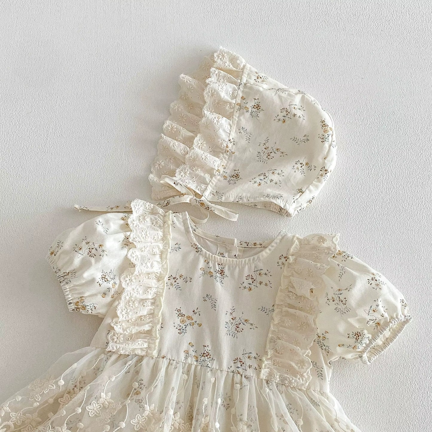 White baby dress with floral pattern and matching bonnet on a light gray background