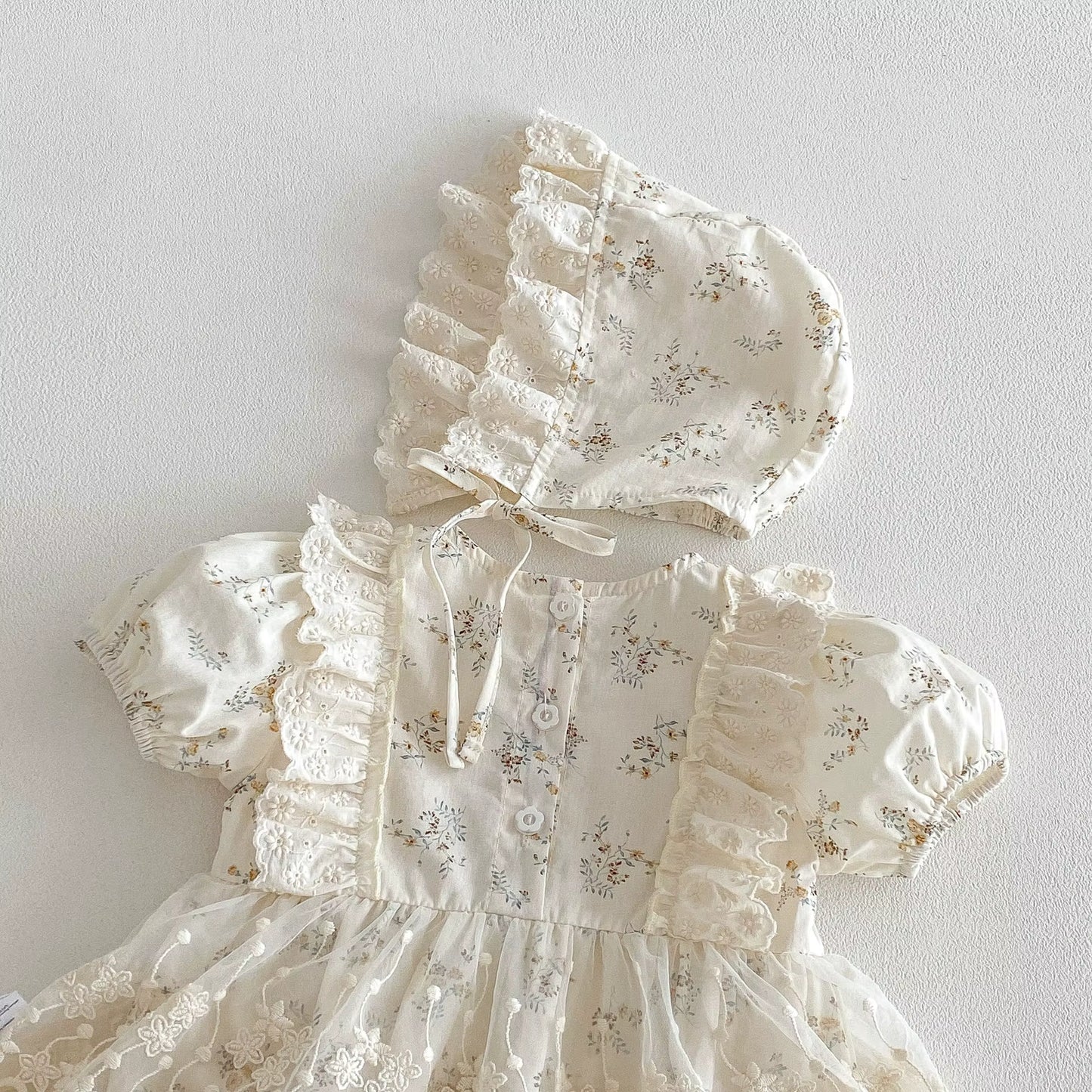 White baby dress with floral patterns and matching bonnet on a light gray background