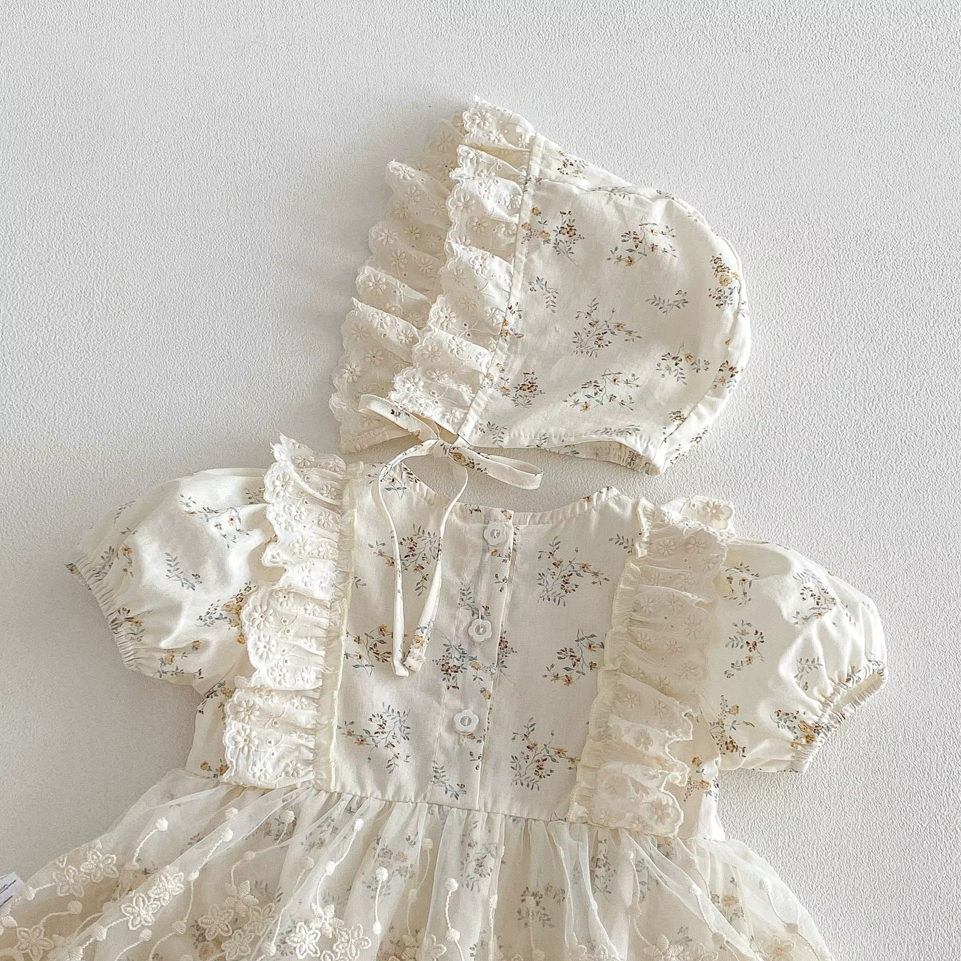 White baby dress with floral patterns and matching bonnet on a light gray background