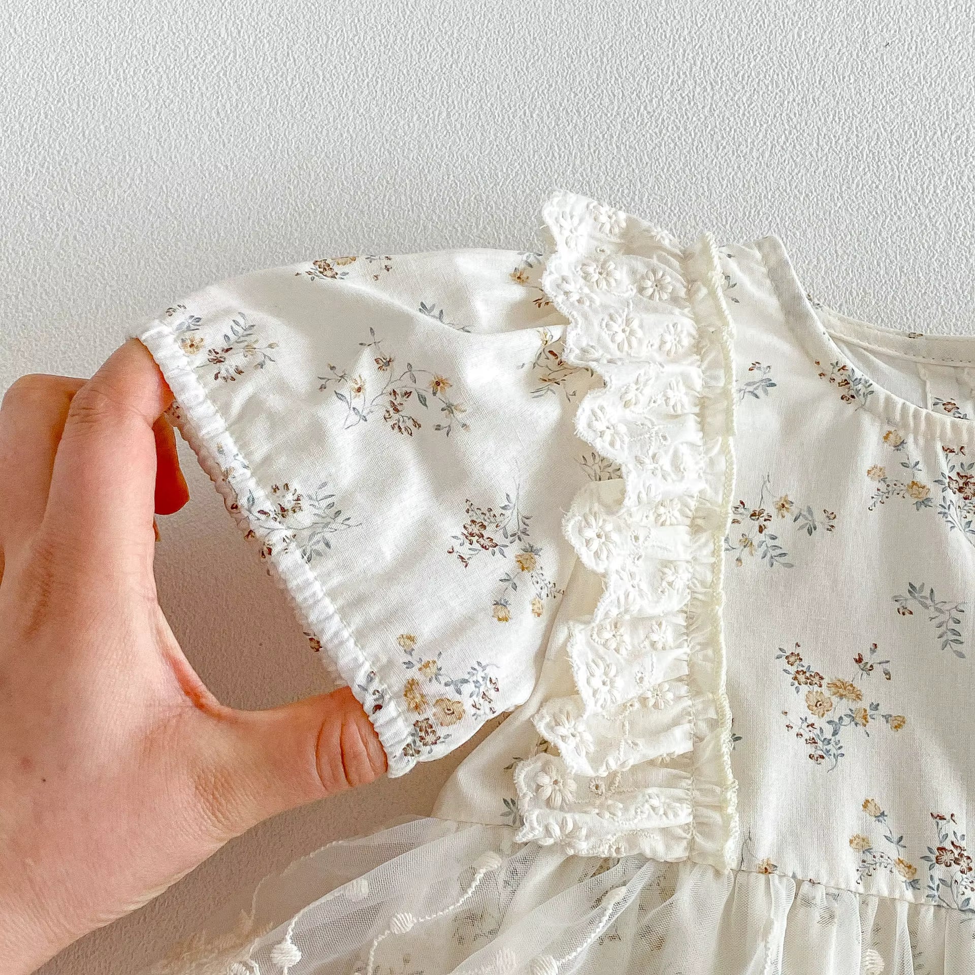 White floral dress with lace details held by a hand against a plain background