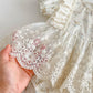 Close-up of a hand holding a piece of lace fabric with a floral dress in the background.