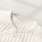 Close-up of a white ribbed knit baby top or bodysuit showing the collar, snap-button closure, and a small star detail on a textured white fabric background.