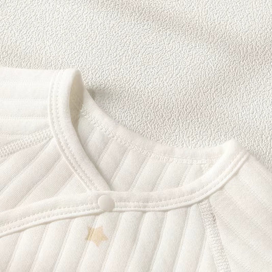 Close-up of a white ribbed knit baby top or bodysuit showing the collar, snap-button closure, and a small star detail on a textured white fabric background.