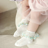 Baby wearing white socks with decorative elements, sitting on a couch.
