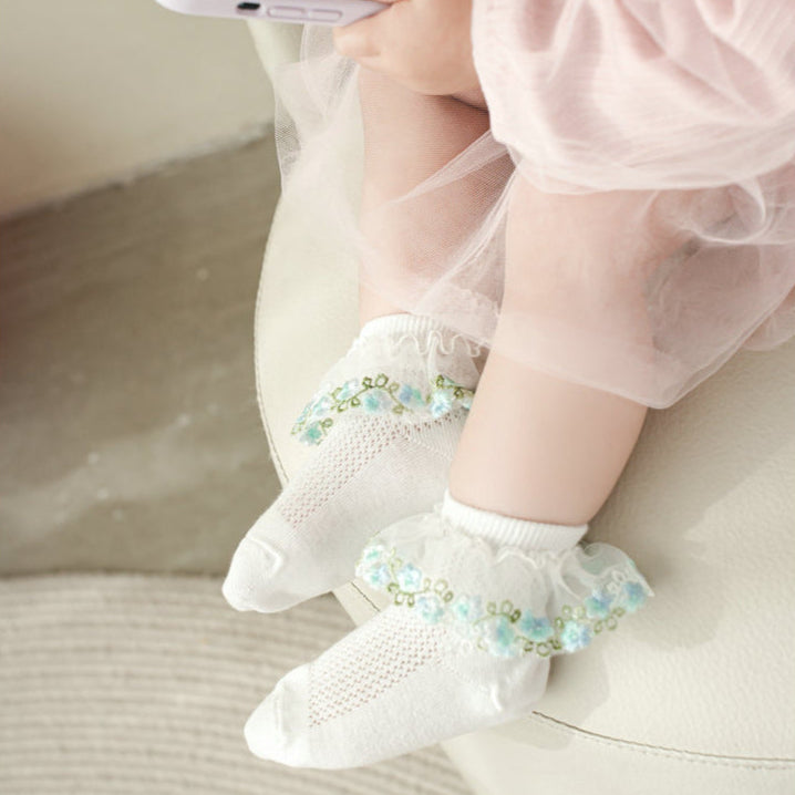 Baby wearing white socks with decorative elements, sitting on a couch.