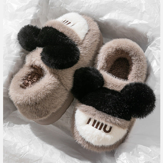 Pair of slippers with fuzzy texture and black pom-poms on a white textured background