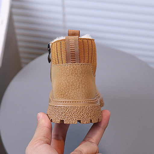 Tan suede boot held in a hand with a blurred indoor background