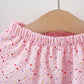 Pink children's pants with heart patterns on a wooden hanger against a white background