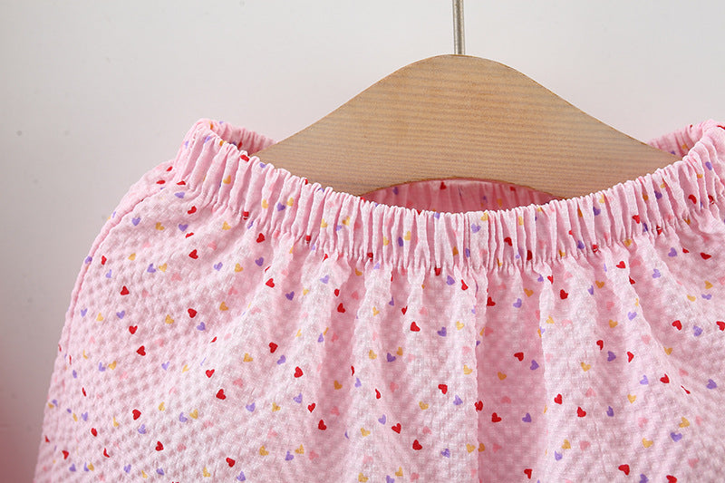 Pink children's pants with heart patterns on a wooden hanger against a white background
