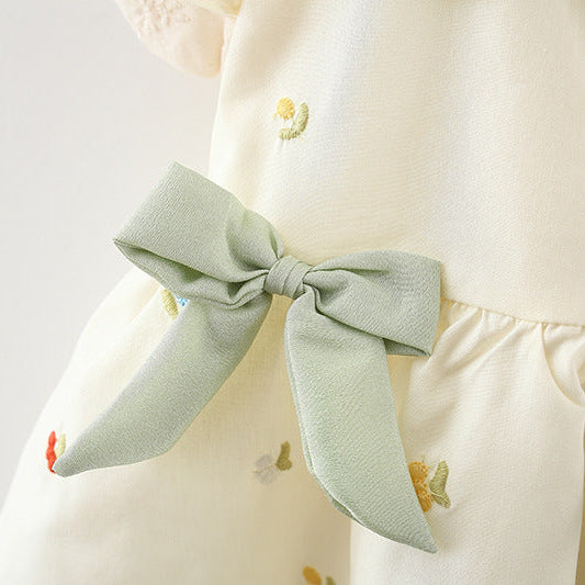 Close-up of a light green bow on a white dress with small colorful designs.